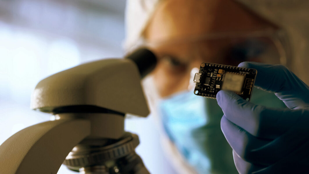 Technician examining chip, using microscope to run diagnosis and upgrade device